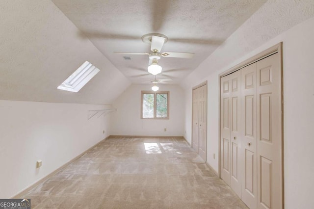 bonus room featuring vaulted ceiling with skylight, ceiling fan, light carpet, and a textured ceiling