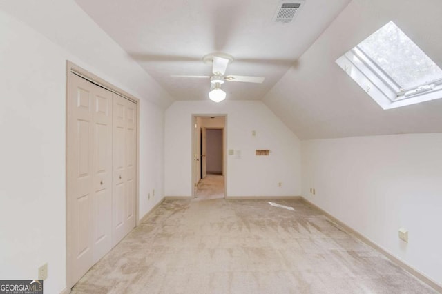 additional living space featuring ceiling fan, vaulted ceiling with skylight, and light colored carpet