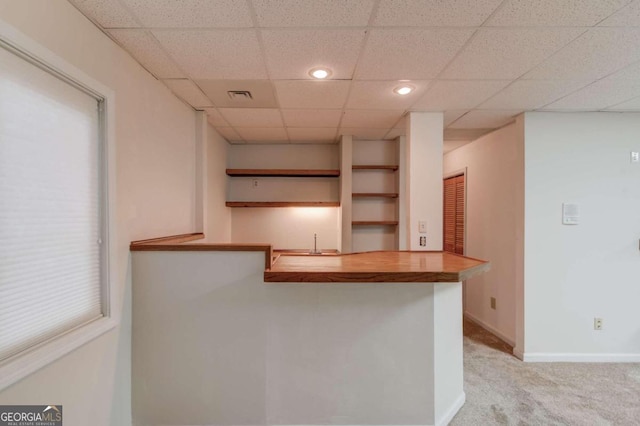 kitchen featuring kitchen peninsula, light colored carpet, butcher block countertops, and a drop ceiling