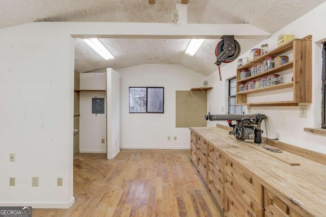 kitchen with a textured ceiling, light hardwood / wood-style floors, lofted ceiling, and electric panel