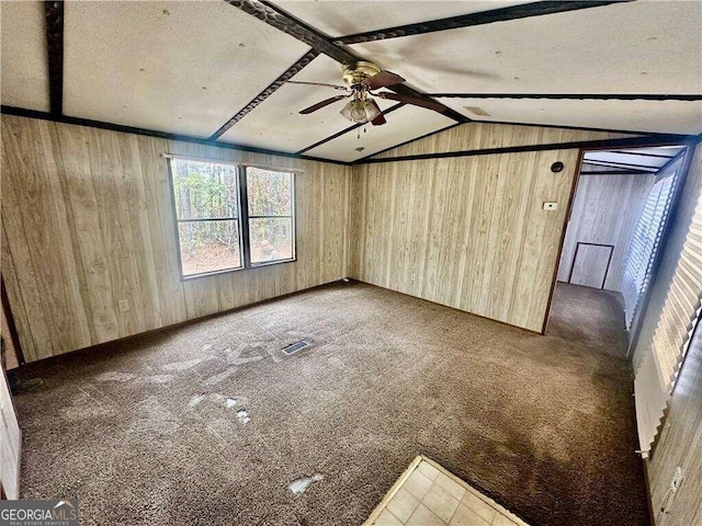 carpeted spare room featuring ceiling fan, wood walls, and lofted ceiling