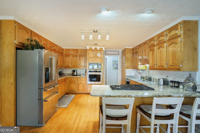 kitchen with kitchen peninsula, appliances with stainless steel finishes, a textured ceiling, sink, and light hardwood / wood-style floors