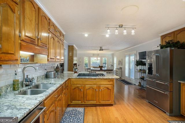 kitchen with sink, light wood-type flooring, ornamental molding, kitchen peninsula, and stainless steel appliances