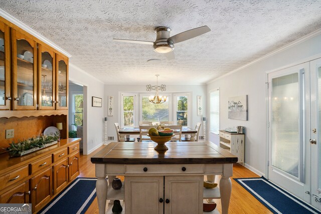 kitchen with a textured ceiling, light wood-type flooring, decorative light fixtures, and ornamental molding