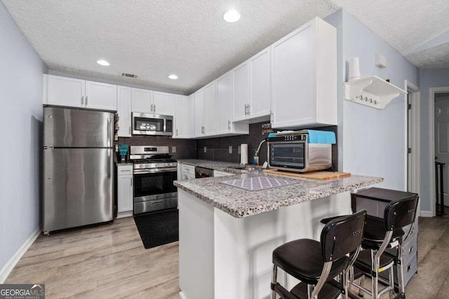 kitchen featuring kitchen peninsula, appliances with stainless steel finishes, light wood-type flooring, a breakfast bar, and white cabinets