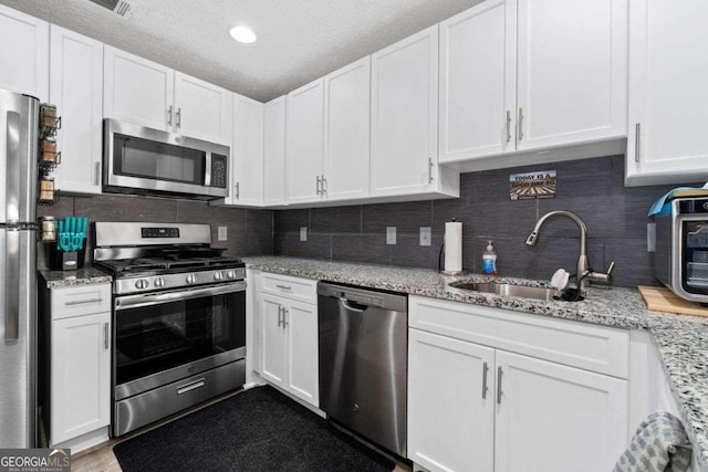 kitchen with sink, light stone countertops, a textured ceiling, appliances with stainless steel finishes, and white cabinetry