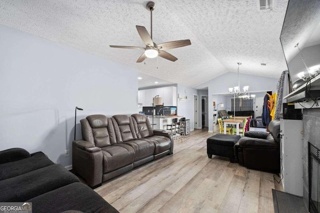 living room featuring ceiling fan with notable chandelier, light wood-type flooring, a textured ceiling, and vaulted ceiling