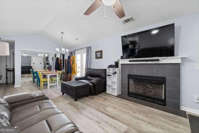 living room featuring lofted ceiling, ceiling fan with notable chandelier, a textured ceiling, a fireplace, and light hardwood / wood-style floors