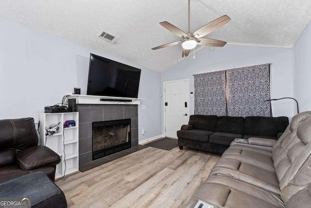 living room with lofted ceiling, hardwood / wood-style flooring, ceiling fan, a textured ceiling, and a tiled fireplace