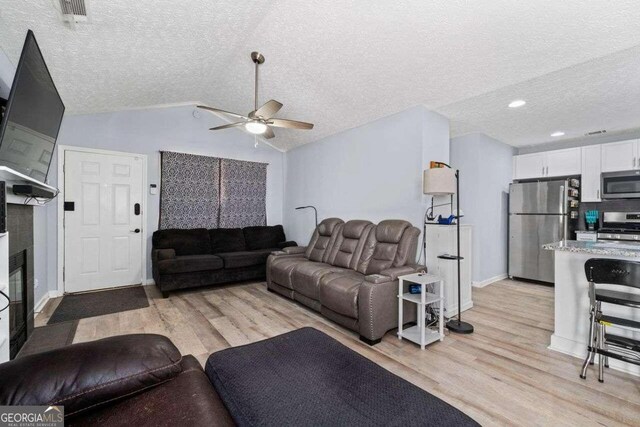 living room with ceiling fan, vaulted ceiling, a textured ceiling, and light hardwood / wood-style flooring