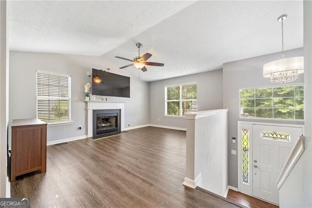 unfurnished living room with dark hardwood / wood-style flooring, ceiling fan with notable chandelier, and lofted ceiling