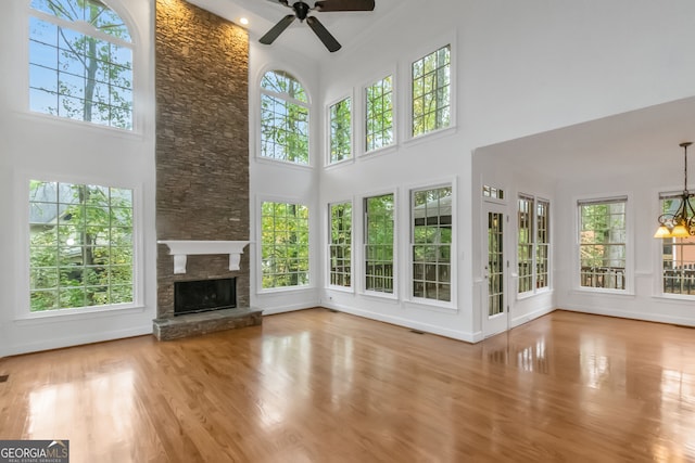 unfurnished living room with a stone fireplace, ceiling fan with notable chandelier, a high ceiling, and hardwood / wood-style flooring