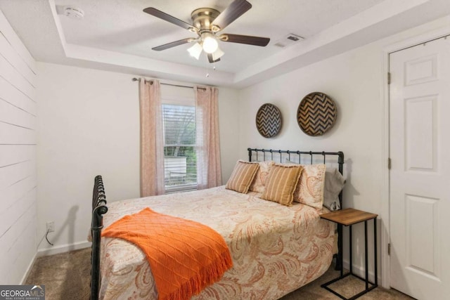 carpeted bedroom with a tray ceiling and ceiling fan