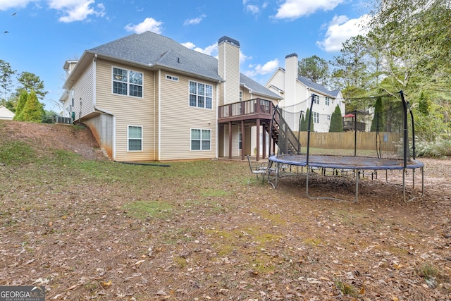 rear view of property with a trampoline and a wooden deck