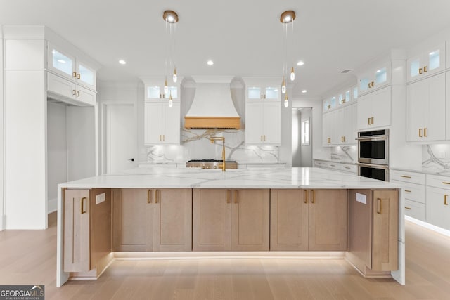 kitchen featuring light stone countertops, custom exhaust hood, double oven, a spacious island, and white cabinets