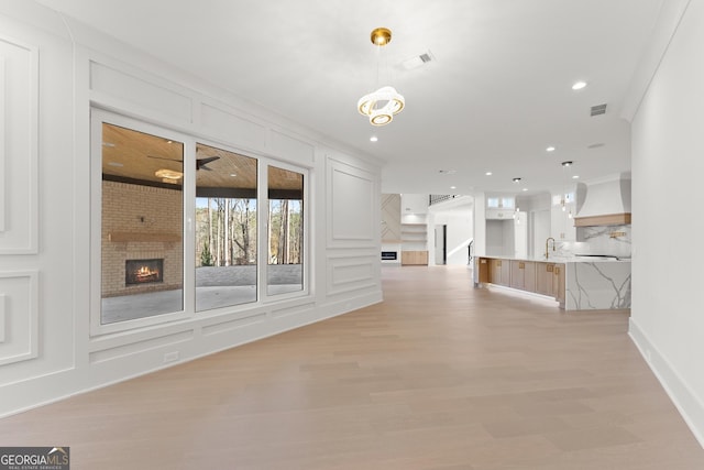 unfurnished living room with crown molding, light hardwood / wood-style flooring, sink, and a brick fireplace