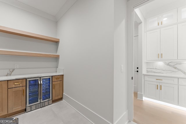 bar with backsplash, white cabinets, wine cooler, light stone countertops, and ornamental molding