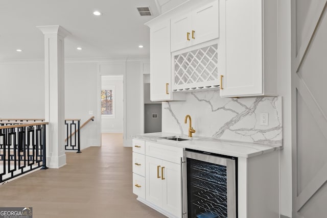 kitchen featuring white cabinets, sink, wine cooler, light stone counters, and decorative columns