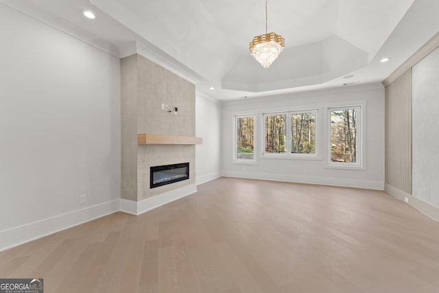 unfurnished living room with a large fireplace, wood-type flooring, a tray ceiling, and an inviting chandelier