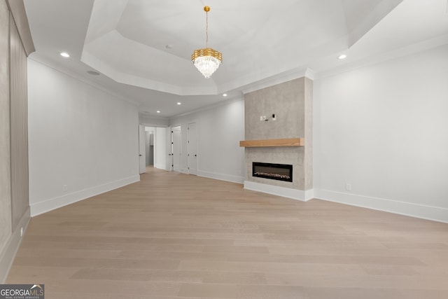 unfurnished living room featuring a large fireplace, a raised ceiling, crown molding, a notable chandelier, and light hardwood / wood-style floors