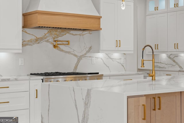 kitchen featuring decorative backsplash, custom range hood, white cabinetry, and light stone counters