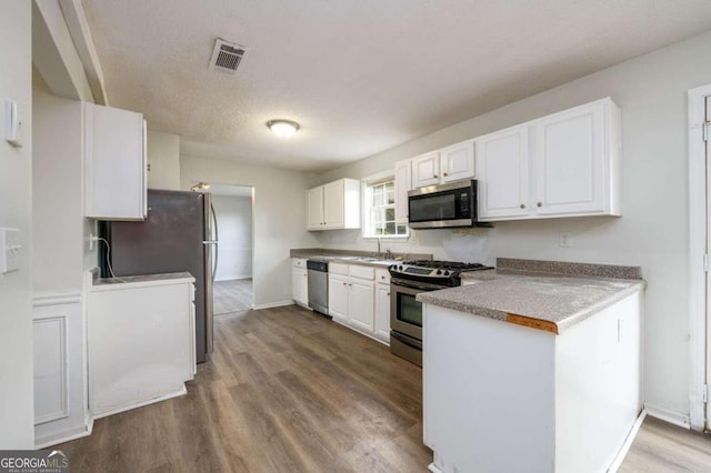 kitchen with white cabinets, stainless steel appliances, hardwood / wood-style flooring, and a textured ceiling