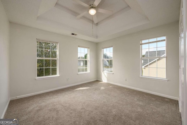 carpeted empty room featuring ceiling fan, a wealth of natural light, and a tray ceiling