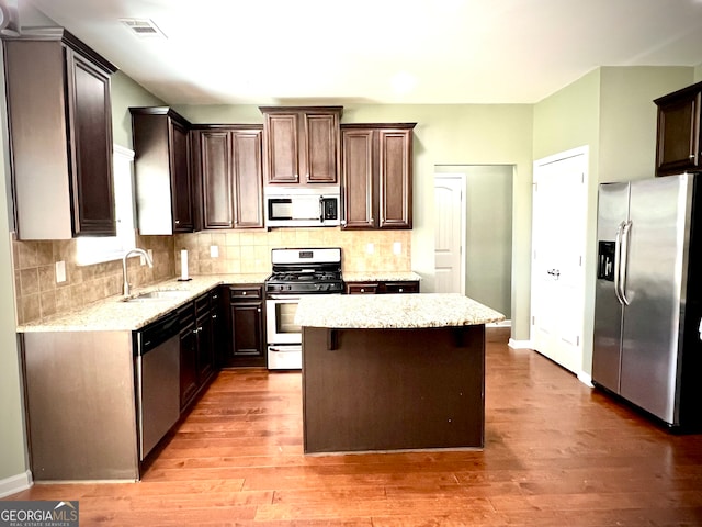 kitchen featuring appliances with stainless steel finishes, dark brown cabinetry, sink, wood-type flooring, and a center island