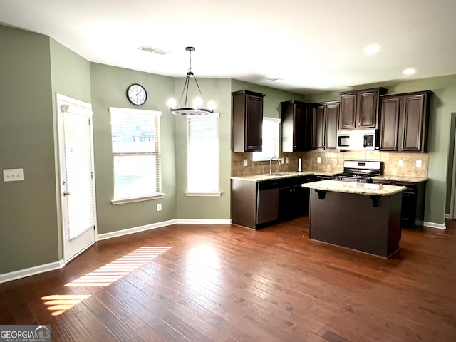 kitchen with pendant lighting, dark wood-type flooring, sink, a kitchen island, and stainless steel appliances