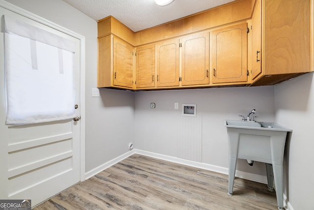 clothes washing area with hookup for a washing machine, cabinets, a textured ceiling, and light hardwood / wood-style flooring