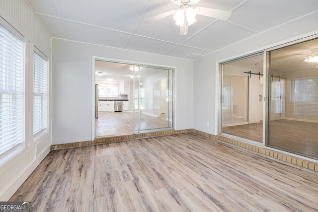 empty room with ceiling fan, a healthy amount of sunlight, a barn door, and light hardwood / wood-style flooring