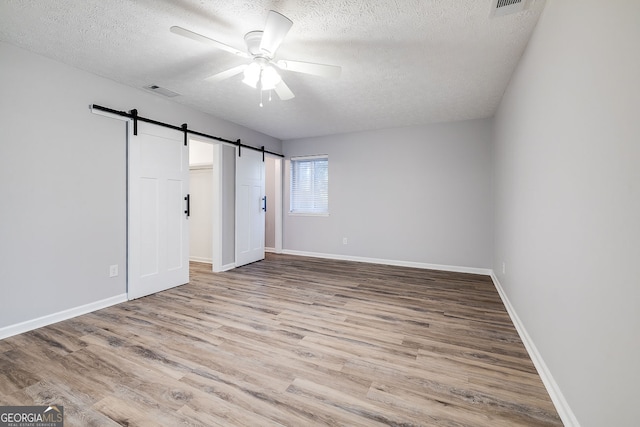 unfurnished bedroom with a barn door, ceiling fan, light hardwood / wood-style floors, and a textured ceiling