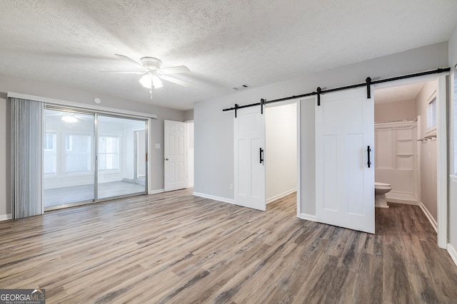 interior space with a barn door, ceiling fan, a textured ceiling, and light wood-type flooring