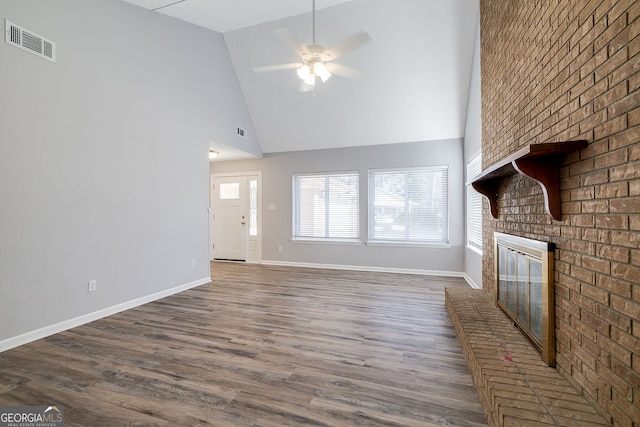 unfurnished living room with a brick fireplace, dark hardwood / wood-style flooring, high vaulted ceiling, and ceiling fan