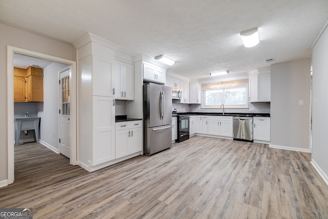 kitchen with light hardwood / wood-style flooring, white cabinets, stainless steel appliances, and a textured ceiling