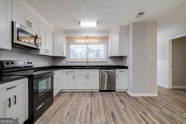 kitchen featuring sink, stainless steel appliances, light hardwood / wood-style floors, a textured ceiling, and white cabinets