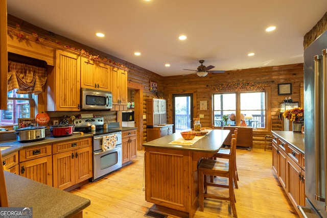 kitchen with a center island, wooden walls, ceiling fan, light hardwood / wood-style floors, and stainless steel appliances