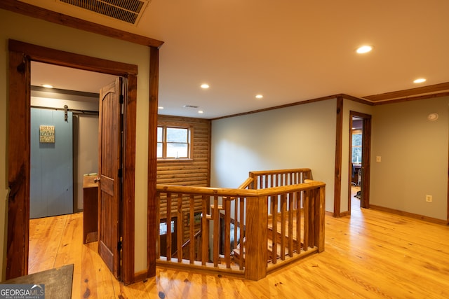 hall with a barn door, light wood-type flooring, and ornamental molding