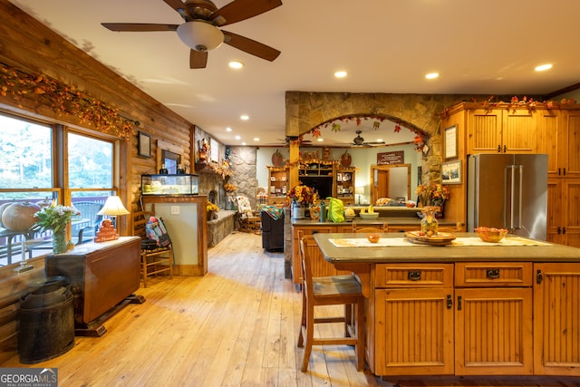 kitchen with ceiling fan, a kitchen breakfast bar, high end fridge, a kitchen island, and light wood-type flooring