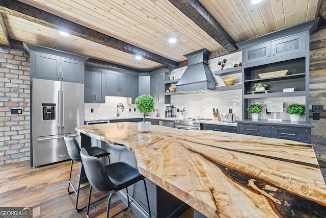 kitchen featuring beam ceiling, wooden ceiling, stainless steel appliances, light hardwood / wood-style flooring, and custom range hood