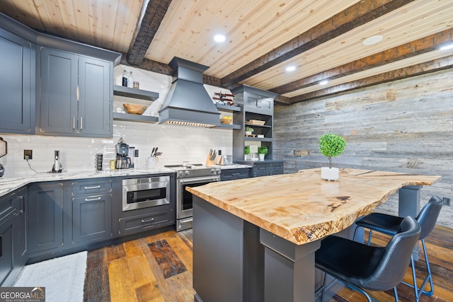 kitchen featuring wood walls, dark wood-type flooring, a kitchen island, beam ceiling, and stainless steel appliances