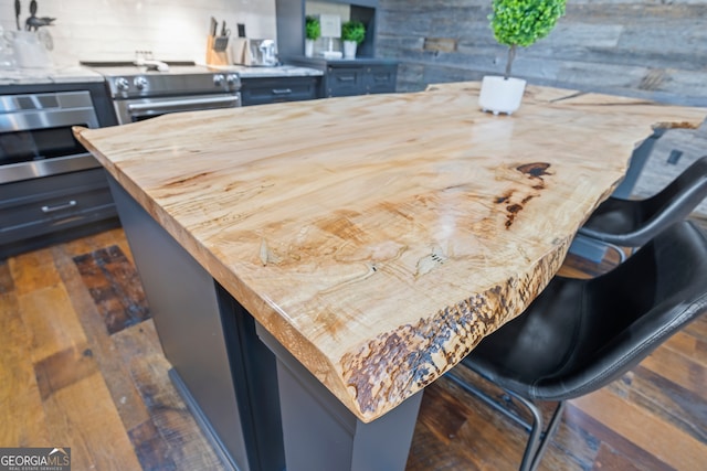 kitchen featuring dark hardwood / wood-style flooring, backsplash, a breakfast bar, stainless steel electric stove, and butcher block counters