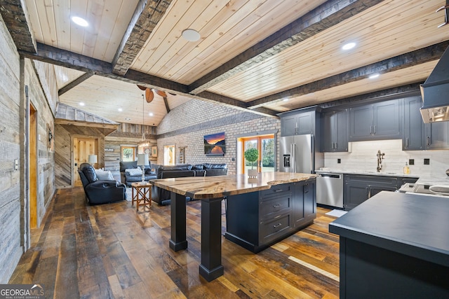 kitchen with appliances with stainless steel finishes, dark hardwood / wood-style flooring, lofted ceiling with beams, and a center island