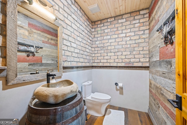 bathroom with wood ceiling, brick wall, vanity, wood-type flooring, and toilet