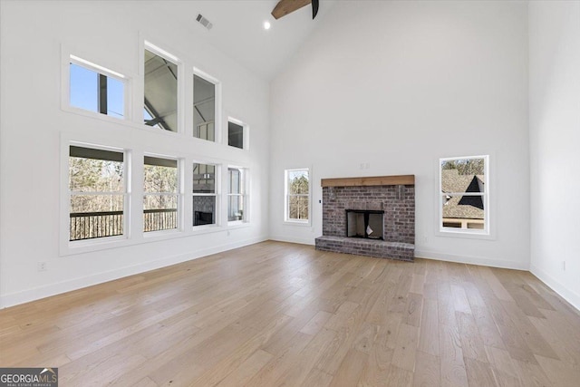 unfurnished living room with a brick fireplace, visible vents, baseboards, and light wood finished floors