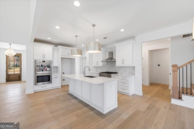 kitchen with double oven, white cabinets, light countertops, and wall chimney range hood