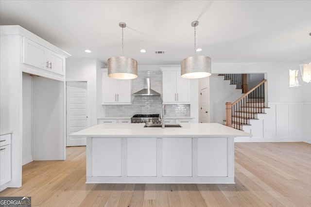 kitchen with an island with sink, wall chimney exhaust hood, pendant lighting, and light countertops