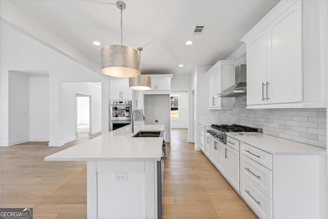 kitchen featuring stainless steel appliances, a sink, light countertops, wall chimney exhaust hood, and decorative light fixtures