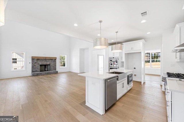 kitchen featuring appliances with stainless steel finishes, light countertops, white cabinets, and a center island with sink