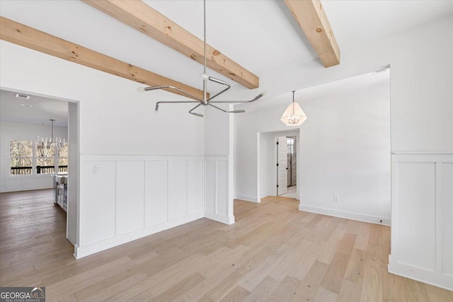 unfurnished dining area featuring beam ceiling, light wood finished floors, a decorative wall, wainscoting, and a chandelier